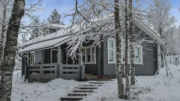 A cabin with a wooden porch, surrounded by snow-covered trees.