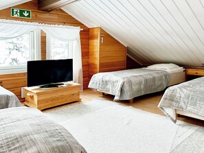 A cozy attic bedroom with a television on a wooden dresser, two single beds, and a window with curtains. - Kallentupa by Interhome (Kuusamo)