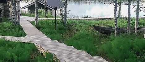 A wooden boardwalk leading to a cabin by a lake with a boat nearby.