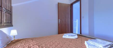 A bedroom with a bed, a nightstand, a lamp, a wooden wardrobe, and a door leading to a balcony.