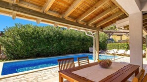 Un espacio al aire libre cubierto con piscina, muebles de madera y suelo de baldosas de piedra.