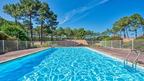 A rectangular swimming pool with clear blue water, surrounded by a white metal fence and trees. - Jardins de la Pinède by Interhome (Lacanau)