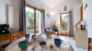 A dining area with a table set for breakfast, a sofa, and a view of the outdoors. - Jardins de la Pinède by Interhome (Lacanau)