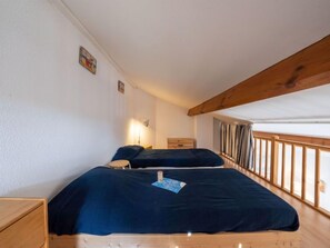 Una camera con due letti, testiere in legno, un comodino e una lampada a parete, oltre a una finestra con tende.
