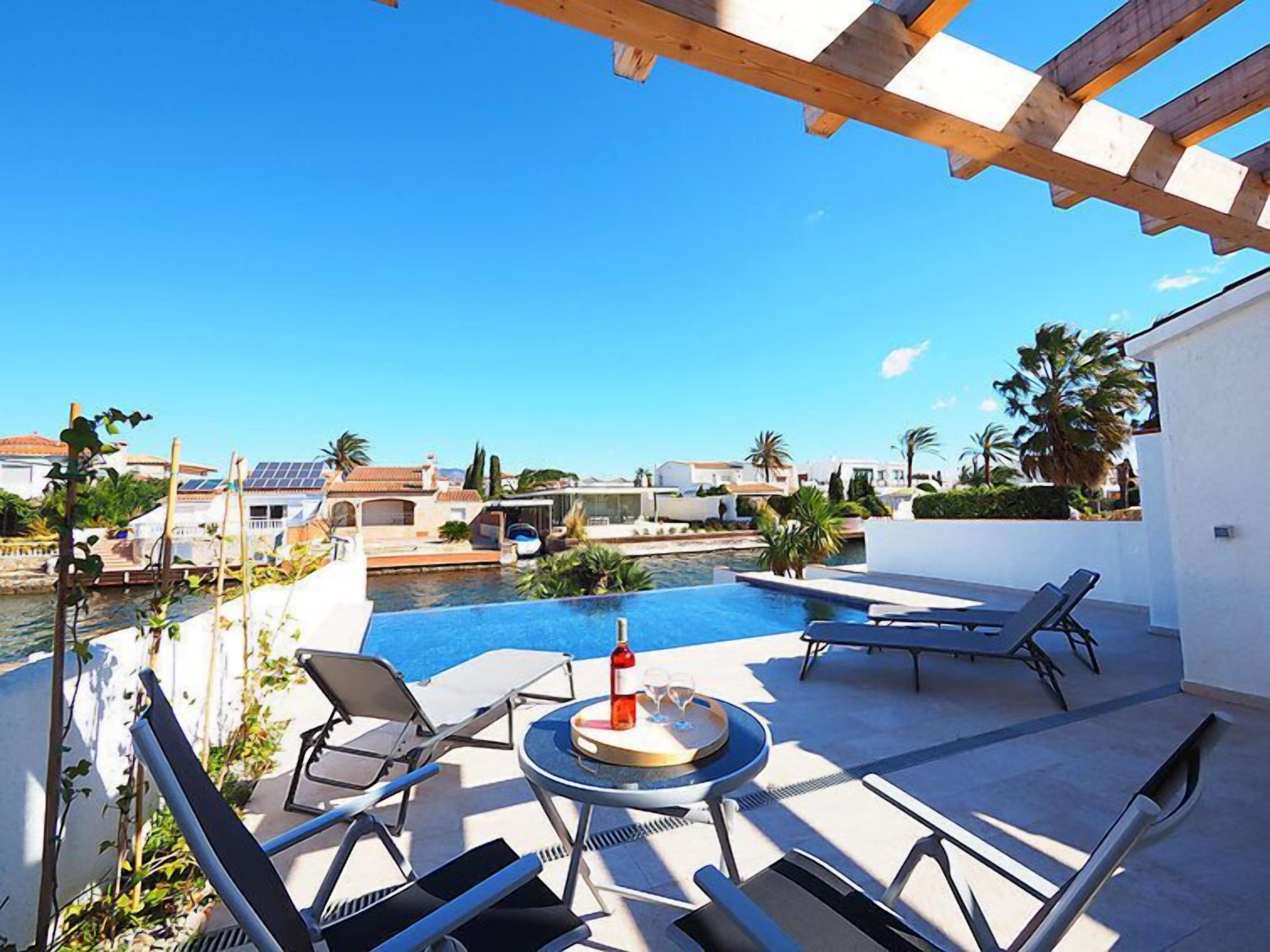 A rooftop pool area with lounge chairs and a table, overlooking a body of water and a residential area.