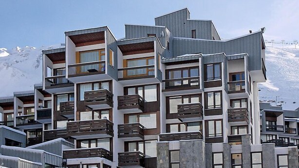 Een hotel met meerdere verdiepingen, balkons, een modern architectonisch ontwerp en een besneeuwde berg op de achtergrond.