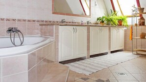A bathroom with a bathtub, a sink, and a mirror. There are cabinets and a potted plant on the counter. - Vacation home Colore by Interhome (Balatonmariafurdo)