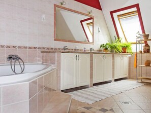 A bathroom with a bathtub, a sink, and a mirror. There are cabinets and a potted plant on the counter. - Vacation home Colore by Interhome (Balatonmariafurdo)