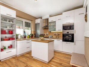 A modern kitchen with white cabinetry, a central island, and built-in appliances including a microwave and oven. - Vacation home Colore by Interhome (Balatonmariafurdo)