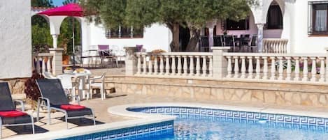 Un área de piscina con sillones de descanso, una pérgola y una zona de comedor con mesas al aire libre.