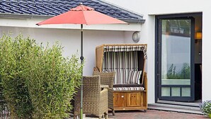 A patio with a wicker chair and a red umbrella, a wooden bench with striped cushions, and a glass door. - Witthuus-Baltrum by Interhome (Norddeich)
