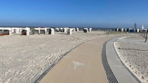 A sandy beach with a curved pathway leading to a series of white structures, possibly beach huts, along the shoreline. - Witthuus-Baltrum by Interhome (Norddeich)