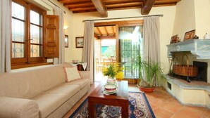 A cozy living room with a beige sofa, wooden ceiling beams, a fireplace, and a view of the outdoors. - Il Girasole by Interhome (Camaiore)