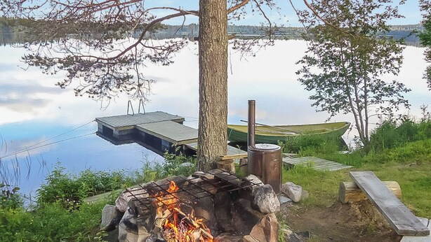 Un feu de camp entouré de rochers, une terrasse en bois et une jetée s’avançant dans un lac.