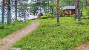 Un sentier de terre mène à un chalet rouge, entouré d’une végétation luxuriante et d’arbres.