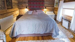 Une chambre à coucher située dans une cabane en rondins, avec un lit, deux tables de chevet, un radiateur et une fenêtre avec des rideaux.