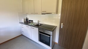 A compact kitchen with white cabinets, a black countertop, a built-in oven, and a wooden door.