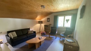 A cozy living room with a wooden ceiling, a sofa, a coffee table, a bookshelf, and a chair.