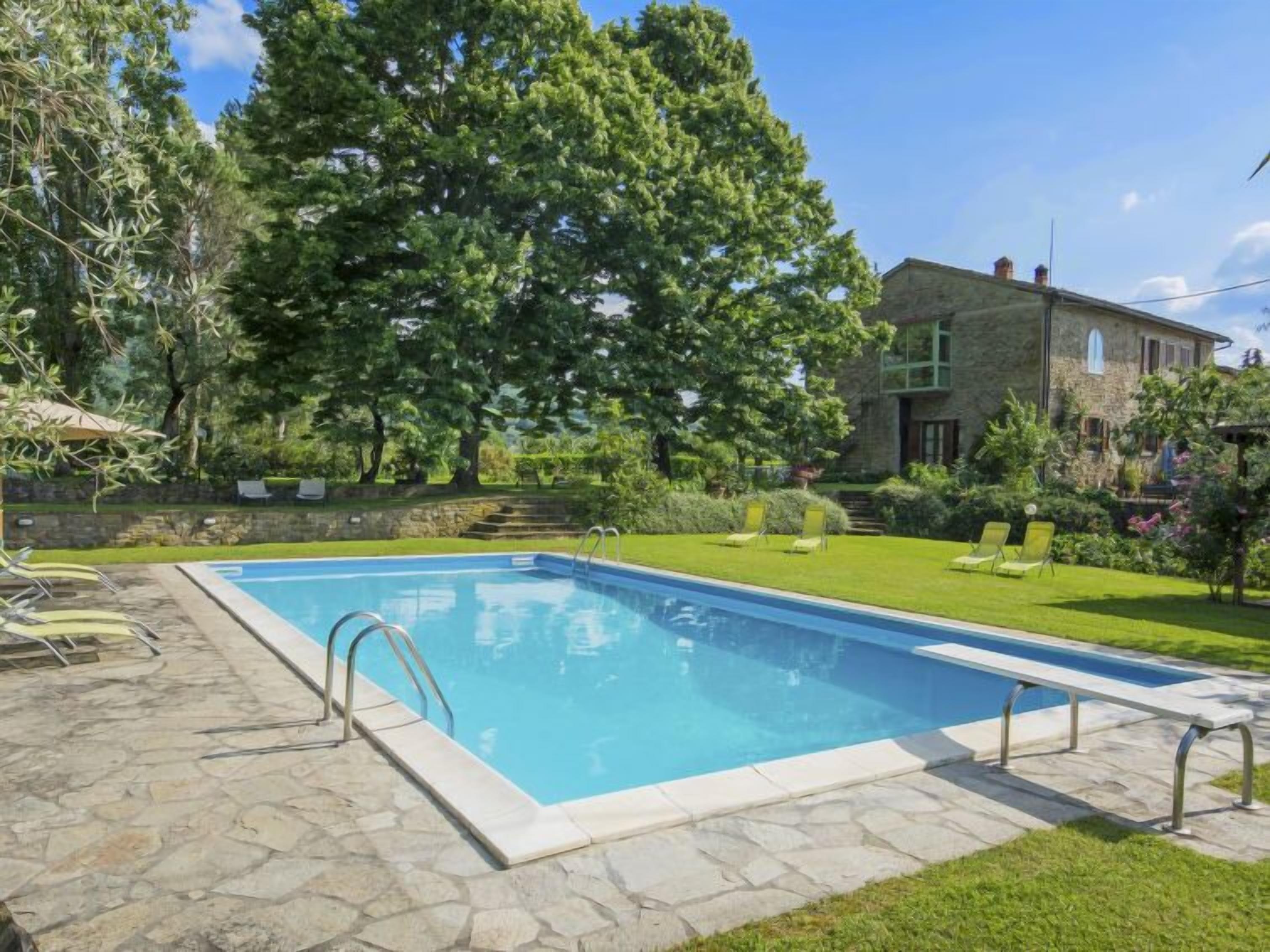 Ein rechteckiger Swimmingpool mit einer Steinterrasse, umgeben von einem gepflegten Rasen und Bäumen.