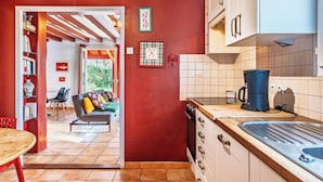 Una cocina con armarios blancos, una máquina de café y un lavabo. Hay un comedor con una mesa y sillas, y un sofá con cojines.