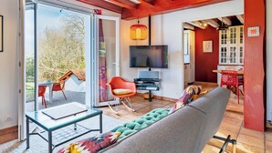 Una sala de estar moderna con un ventanal que da a un balcón, un sofá, un televisor y una zona de comedor con sillas rojas.