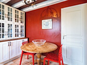 Un coin repas avec une table ronde en bois, des chaises rouges et des meubles blancs dotés de portes en verre.