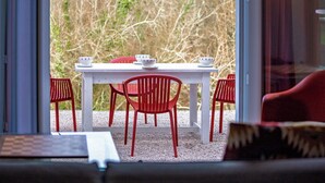 Comedor con una mesa blanca y sillas rojas, visto a través de un vidrio.