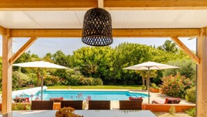 Ein überdachter Außenbereich mit Pool, Holzmöbeln und Sonnenschirmen.