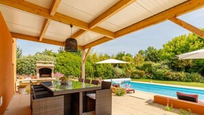 Eine Terrasse im Freien mit Tischplatte aus Glas, Korbstühlen, einem Grill und einem Schwimmbecken.