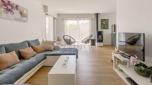 Ein modernes Wohnzimmer mit einem grauen Sofa, einem weißen Couchtisch und einem Fernseher auf einem Standfuß.