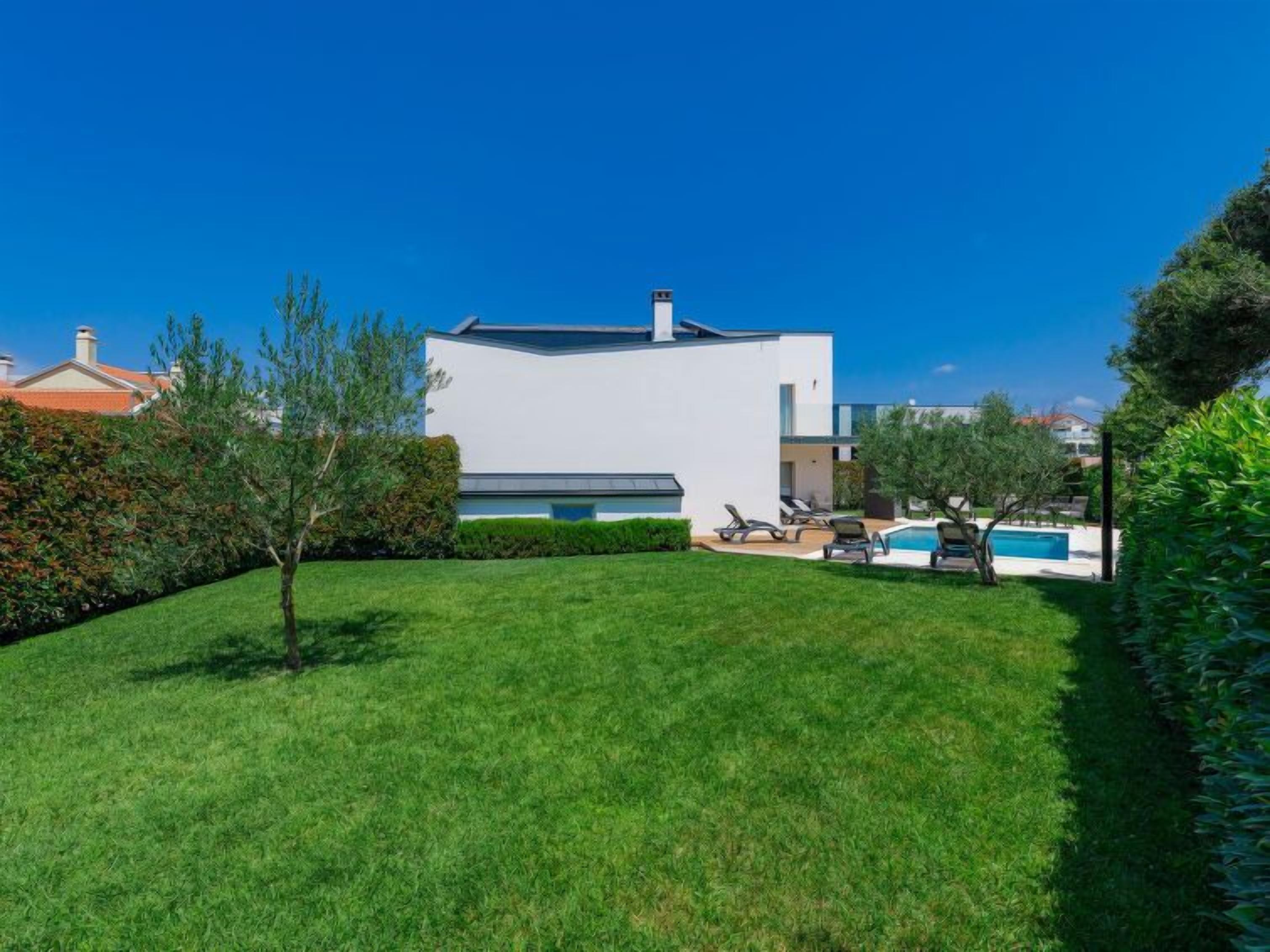 A modern two-story house with a swimming pool, surrounded by well-maintained lawns and trees.