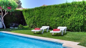 Ein Swimmingpool mit zwei weißen Liegestühlen und roten Handtüchern, umgeben von einer ordentlich geschnittenen Hecke.