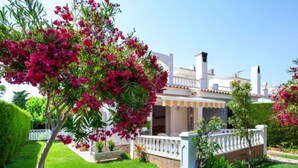 Ein Wohnhaus mit gepflegtem Garten, weißem Zaun und einer kleinen Veranda mit Ziegeldach.