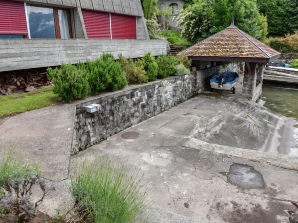 A stone wall with a small gazebo, a concrete patio, and a building with red shutters in the background.