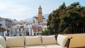 A balcony with a beige sofa, a potted plant, and a basket of fruit.