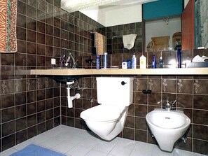Baño con inodoro, bidé y lavamanos, con azulejos marrón oscuro y diseños florales.