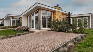 A modern house with a brick pathway leading to the entrance, surrounded by greenery and a clear sky. - Green Resort Mooi Bemelen by Interhome (Bemelen)