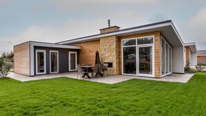 A modern house with a stone facade, large sliding glass doors, and a patio with outdoor furniture. - Green Resort Mooi Bemelen by Interhome (Bemelen)