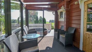 Een overdekt terras met rieten meubels en een glazen tafel, met uitzicht op een groen landschap.