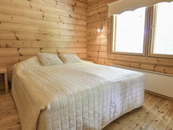 A wooden-paneled room with a bed, a window, and a radiator. - Kannelpirtti 2 by Interhome (Liperi)