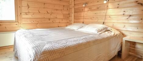A wooden room with a bed, a nightstand, and a lamp.