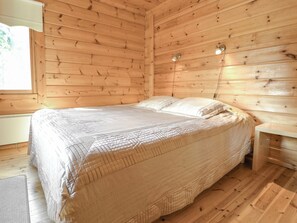 A wooden room with a bed, a nightstand, and a lamp. - Kannelpirtti 2 by Interhome (Liperi)