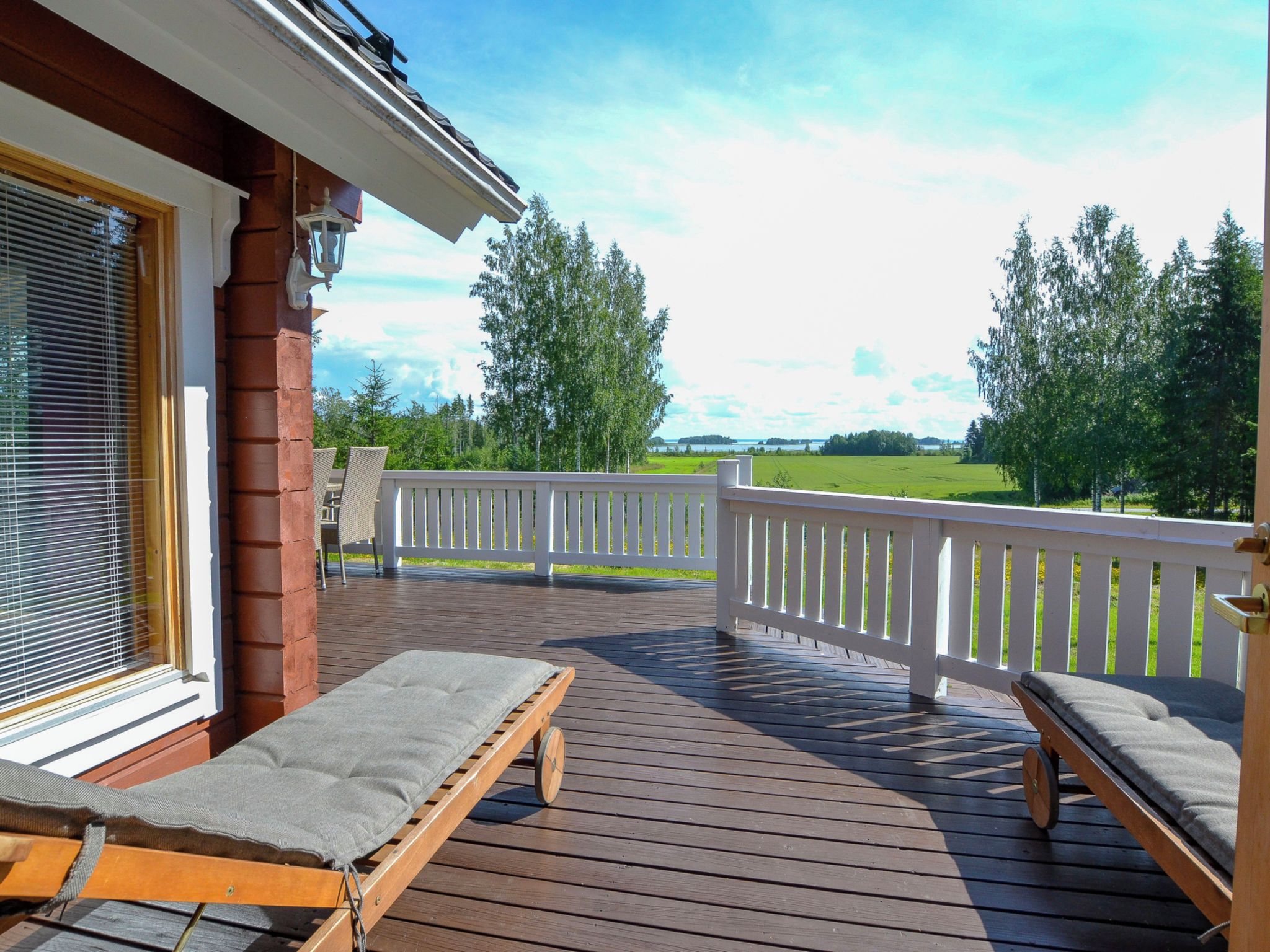 A wooden deck with two lounge chairs and a view of a green landscape.