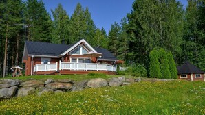 A cabin with a balcony, surrounded by a stone wall and a field of yellow flowers. - Kannelpirtti 2 by Interhome (Liperi)