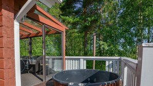 A hot tub on a wooden deck with a glass enclosure and outdoor furniture. - Kannelpirtti 2 by Interhome (Liperi)