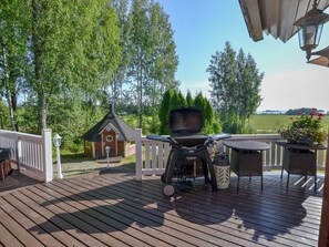 Una terraza de madera con una parrilla, un pequeño edificio y vistas a un paisaje verde.