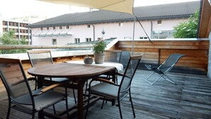 Ulkoterassi, jossa on pyöreä pöytä ja tuoleja, ruukussa oleva kasvi ja näkymä taustalla oleviin rakennuksiin.