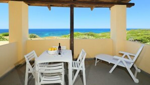 Ein überdachter Außenbereich mit Tisch und Stühlen, mit Blick auf Strand und Meer.