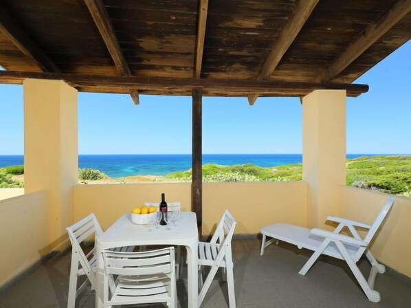 A covered outdoor seating area with a table and chairs, overlooking a beach and ocean.