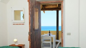Ein Zimmer mit zwei grünen Betten, einer Holztür, die auf einen Balkon mit Tisch und Stühlen führt, und einem kleinen Fenster mit Spiegel.